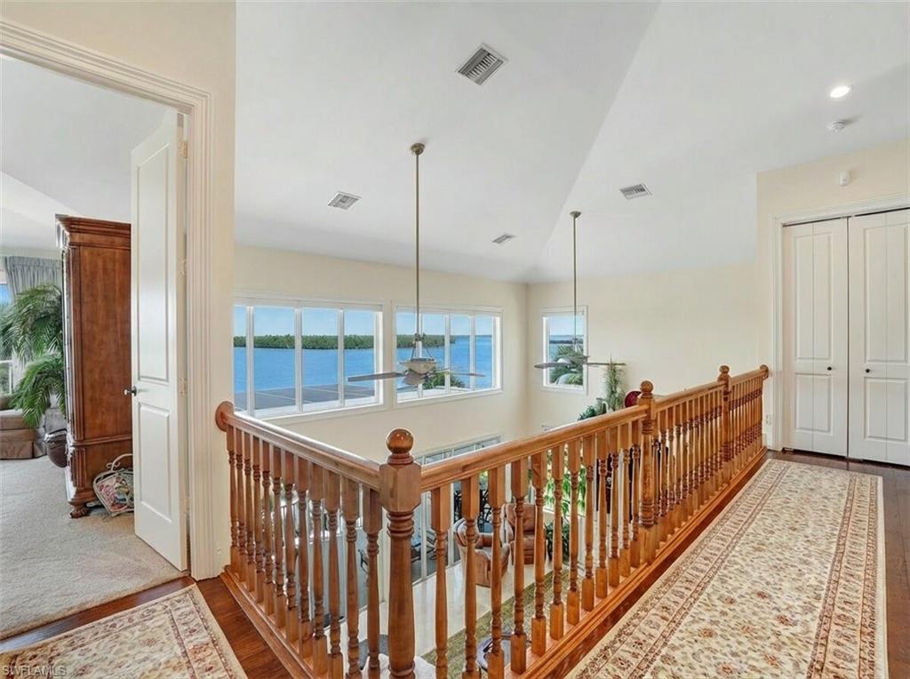 Hall with wood finished floors, an upstairs landing, a water view, and plenty of natural light - Virtually Edited Image