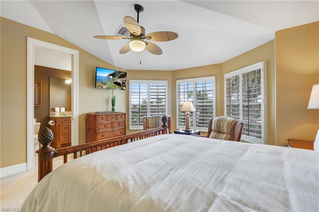 Bedroom featuring light carpet, ceiling fan, vaulted ceiling, and ensuite bath - Virtually Edited Image
