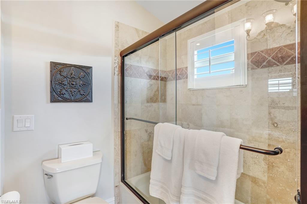 Full bathroom featuring toilet and bath / shower combo with glass door - Virtually Edited Image