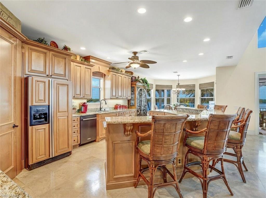 Kitchen featuring light stone countertops, paneled fridge, a breakfast bar, a ceiling fan, and stainless steel dishwasher - Virtually Edited Image
