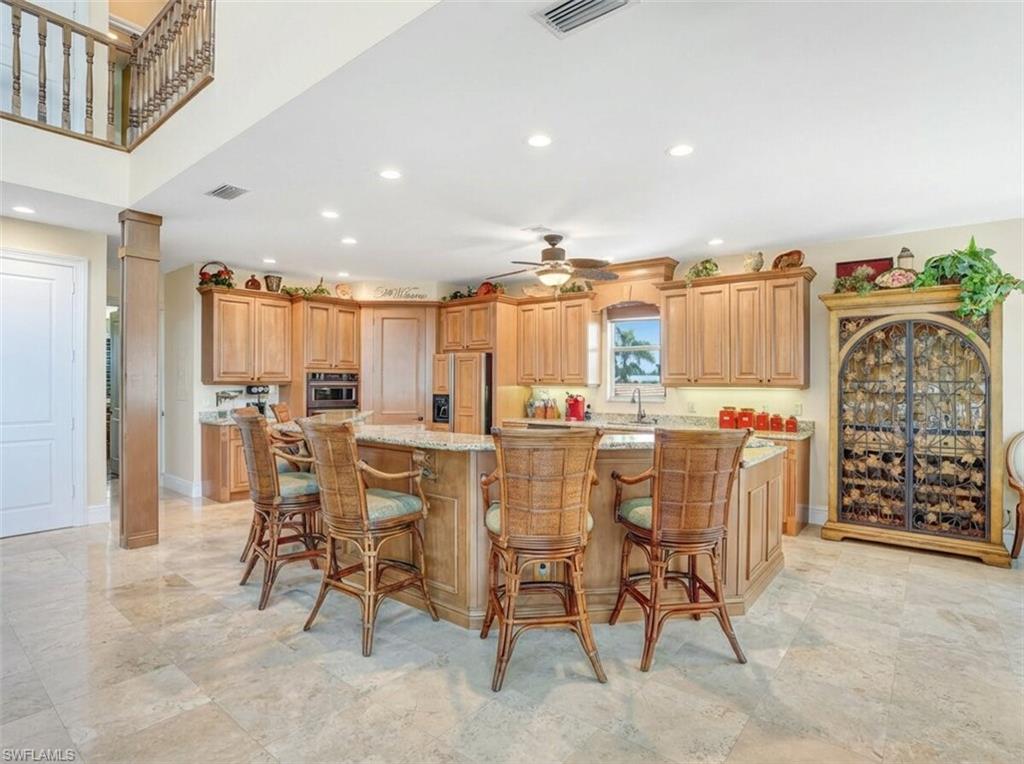 Kitchen with a kitchen breakfast bar, a large island, recessed lighting, light stone countertops, and paneled refrigerator - Virtually Edited Image
