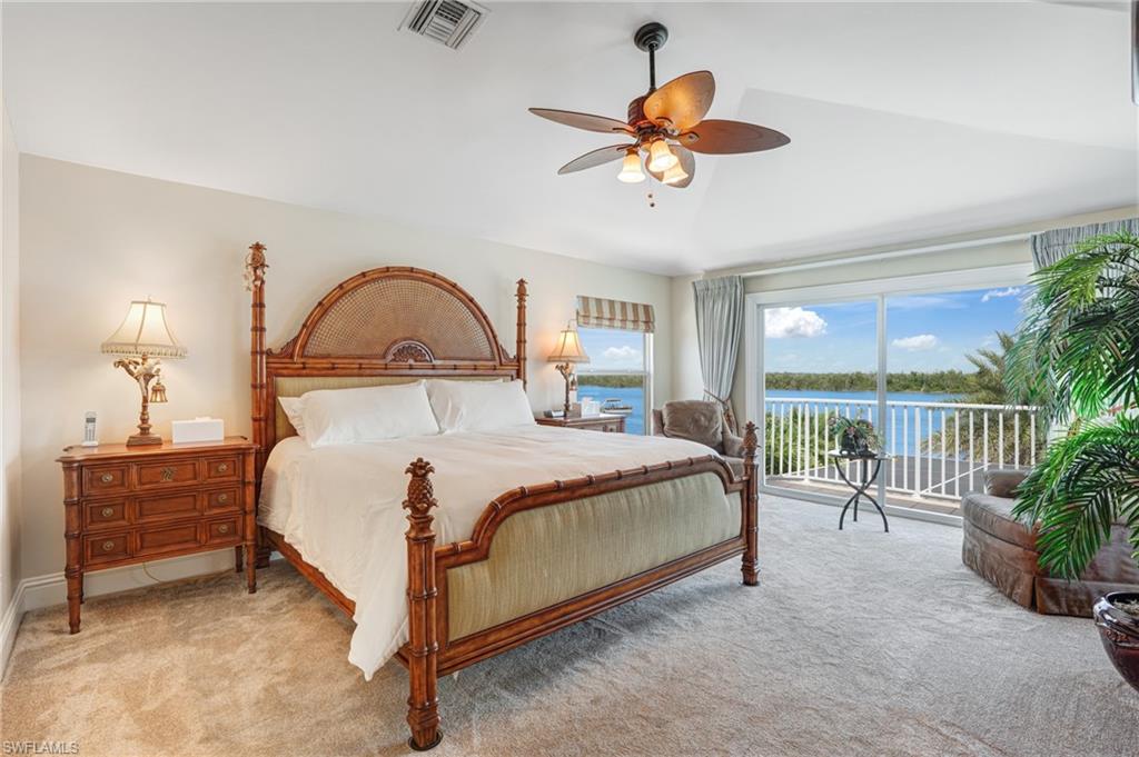 Carpeted bedroom featuring access to exterior, a water view, a ceiling fan, and vaulted ceiling - Virtually Edited Image