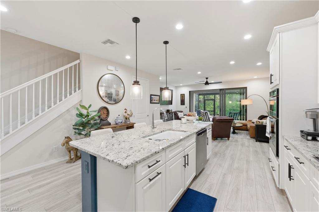 Kitchen with white cabinets, light stone countertops, open floor plan, light wood finished floors, and a ceiling fan