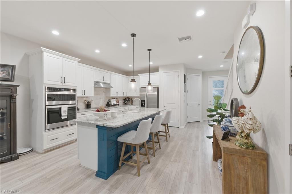 Kitchen featuring white cabinets, light stone countertops, stainless steel appliances, a breakfast bar area, and light wood-type flooring