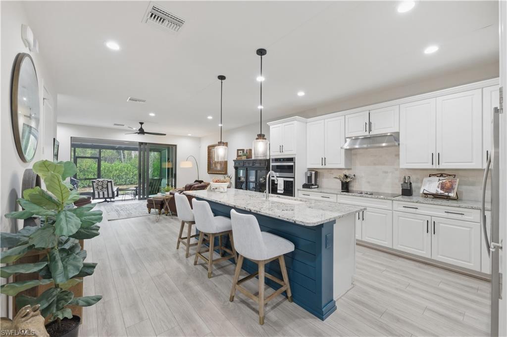 Kitchen featuring white cabinetry, open floor plan, light stone countertops, hanging light fixtures, and a kitchen island with sink