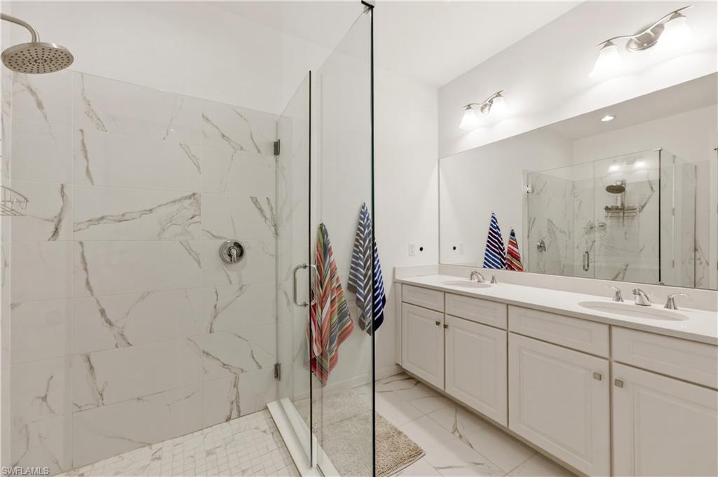 Bathroom featuring double vanity, a marble finish shower, and light marble finish flooring