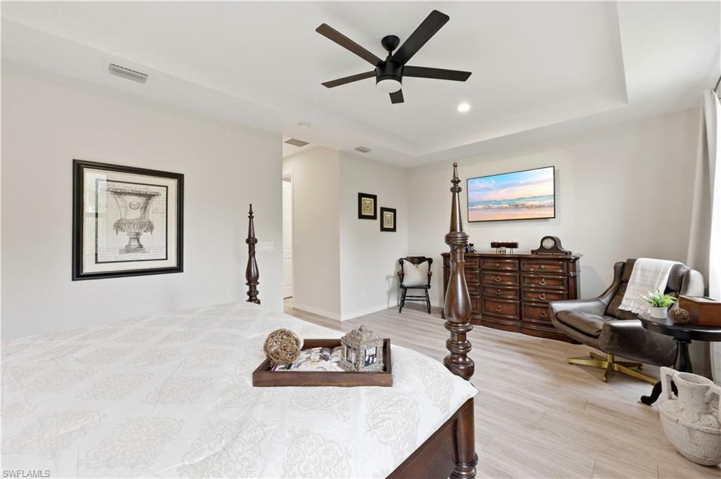 Bedroom with light wood finished floors, a tray ceiling, a ceiling fan, and recessed lighting