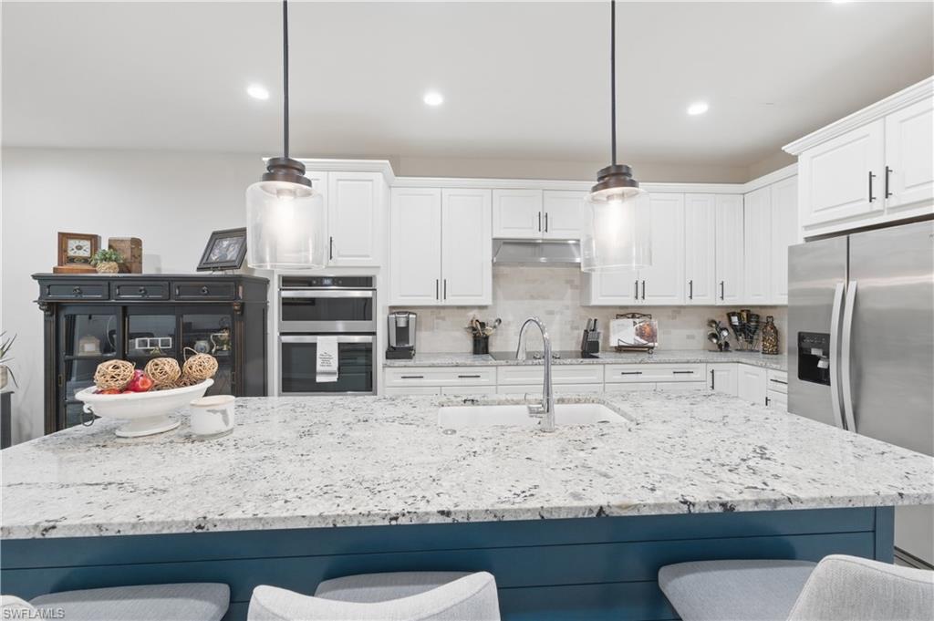 Kitchen with a breakfast bar area, light stone countertops, stainless steel appliances, a kitchen island with sink, and backsplash
