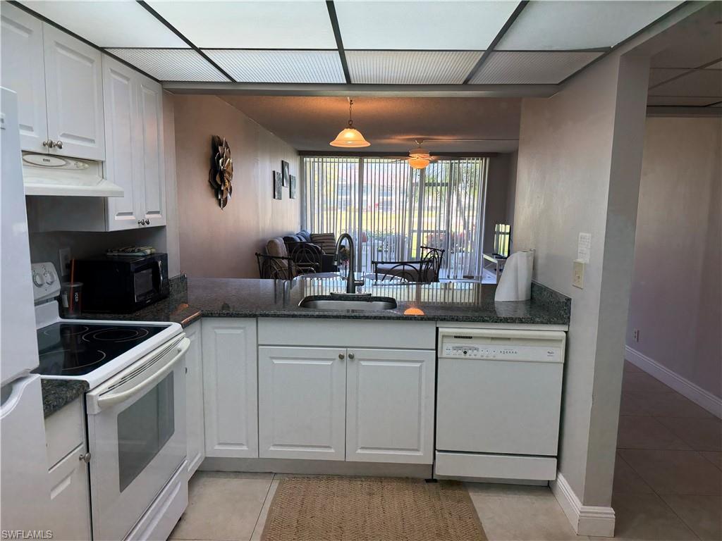 Kitchen featuring light tile patterned floors, white appliances, and white cabinets