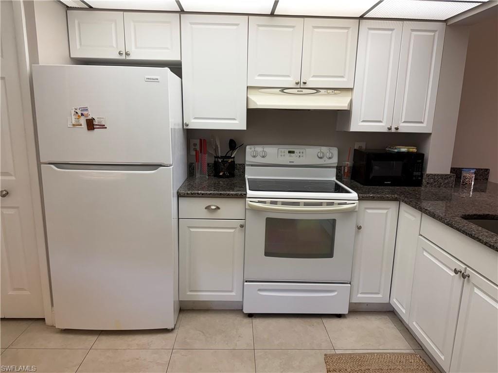 Kitchen featuring white appliances, dark stone countertops, white cabinets, and light tile patterned floors