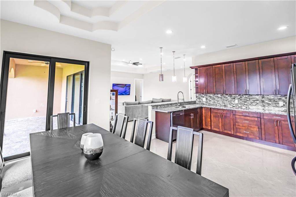 Open-concept dining area featuring a tray ceiling, sliding glass doors to the patio, and a spacious kitchen with dark wood cabinetry, light-toned countertops, and a patterned backsplash