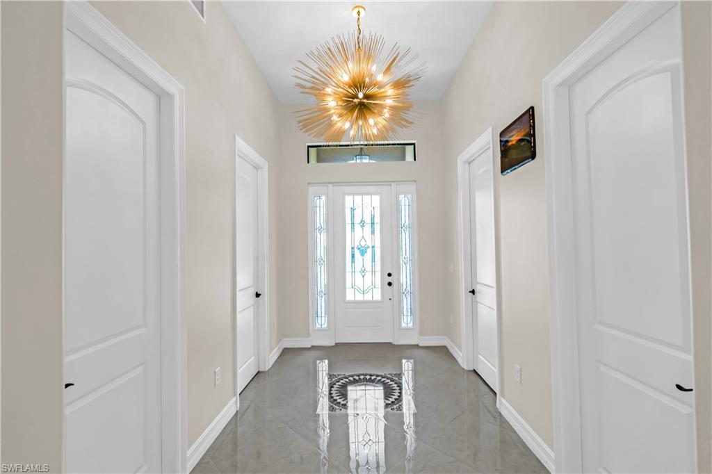 Entryway featuring glossy gray tile flooring, a decorative inlaid floor medallion, and a prominent sputnik-style chandelier