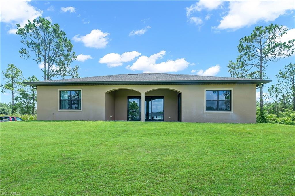 Expansive green lawn with a stucco exterior featuring a covered patio with arched openings and dual glass doors