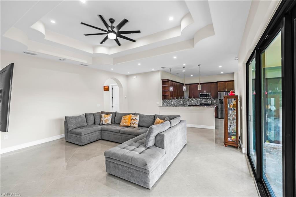 Contemporary living space featuring light tile flooring, a tray ceiling with recessed lighting, and a modern ceiling fan