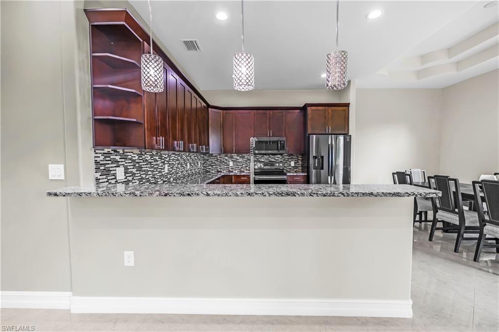 Kitchen featuring dark wood cabinetry, a mosaic tile backsplash, stainless steel appliances, and a breakfast bar with stone countertops