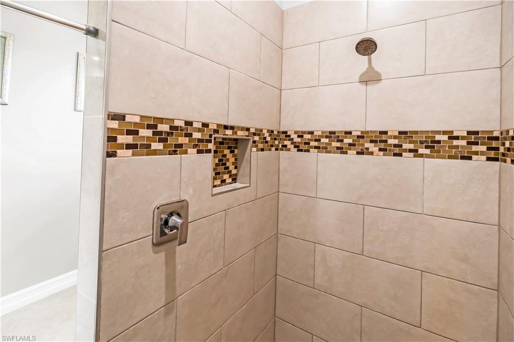 Tiled shower enclosure featuring a mosaic accent band, recessed niche, and a fixed showerhead with a single handle control