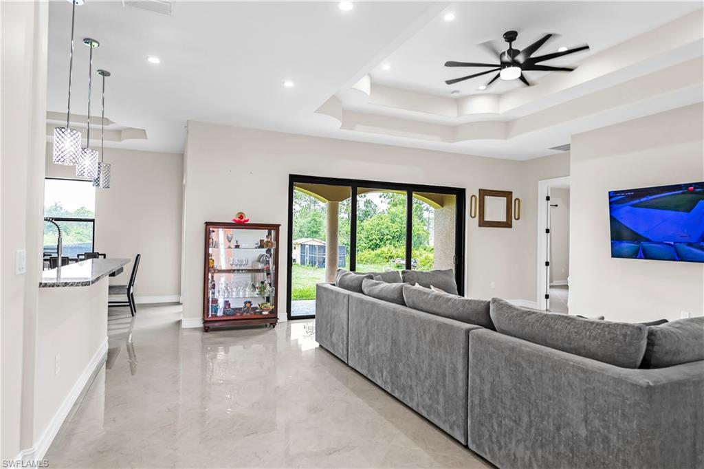 Open-concept living area featuring light-toned flooring, recessed lighting, and a tray ceiling with a contemporary fan