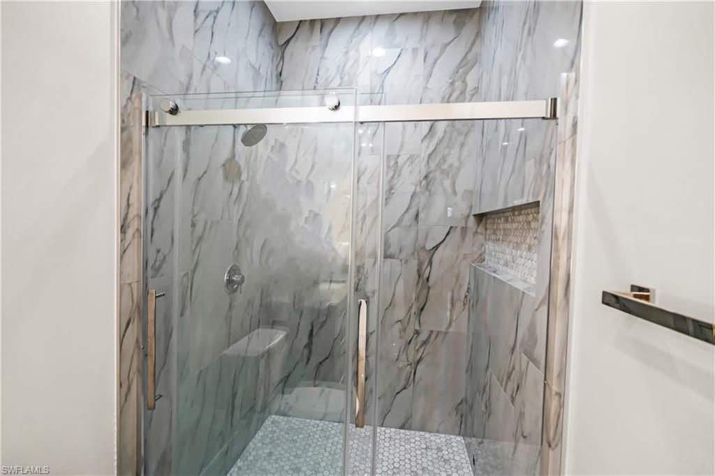 Glass-enclosed shower with a sliding door, featuring large-format marbled wall tiles, a built-in tiled niche, and a contrasting penny tile shower floor