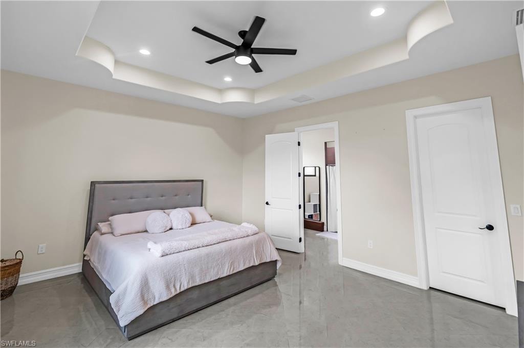 Recessed lighting illuminating a tray ceiling with a contemporary ceiling fan, light-toned walls, and grey-toned tile flooring