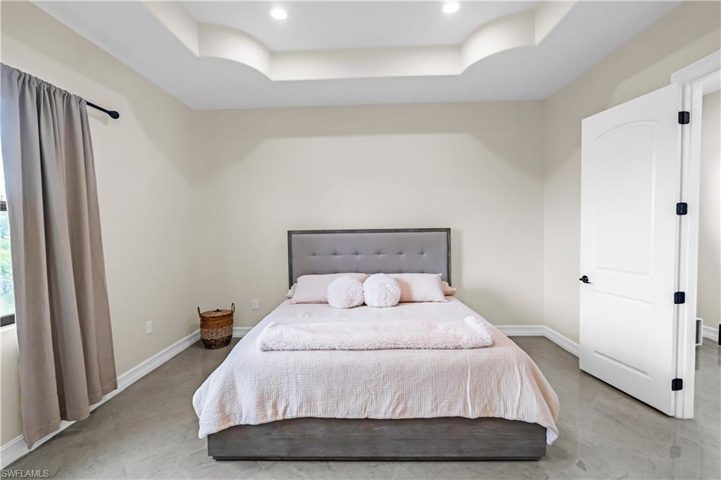 Bedroom featuring a tray ceiling with recessed lighting, light-toned walls, and wood-finish flooring