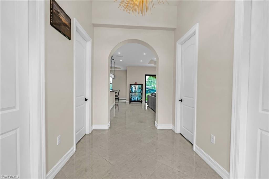 Polished tile flooring extending through a hallway with white paneled doors, an arched entryway, and a contemporary ceiling fixture