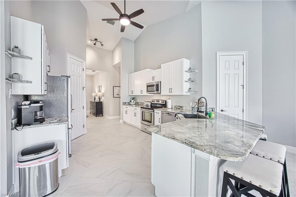 Kitchen with open shelves, a peninsula, white cabinetry, stainless steel appliances, and track lighting