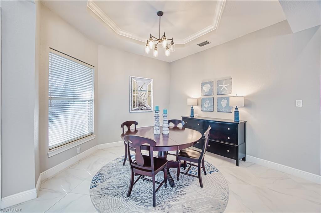 Dining space featuring a tray ceiling, hanging lights, ornamental molding, and light marble finish floors