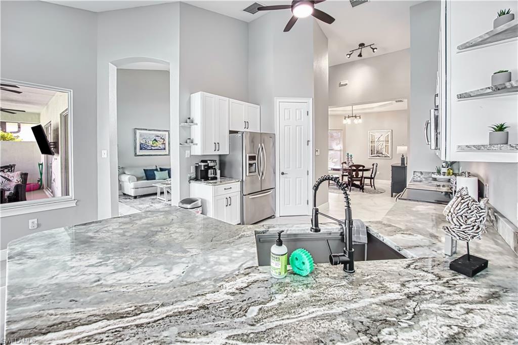 Kitchen with a ceiling fan, open shelves, light stone countertops, white cabinets, and stainless steel appliances