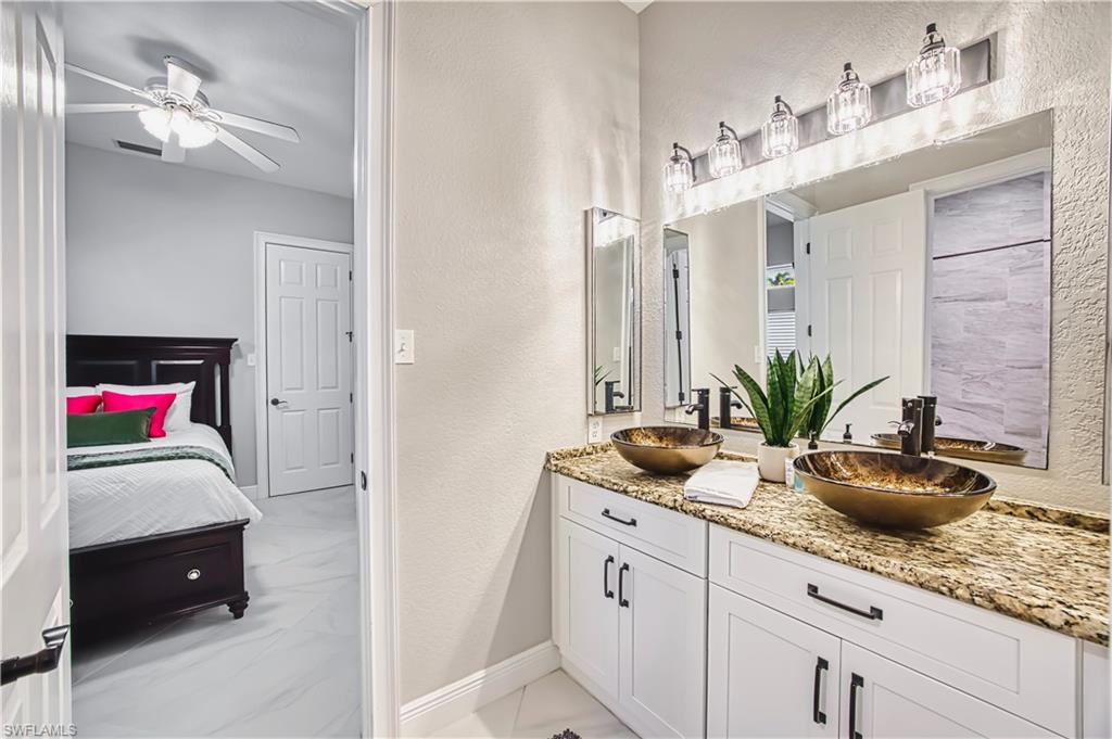 Ensuite bathroom featuring a textured wall, double vanity, a ceiling fan, and light marble finish floors