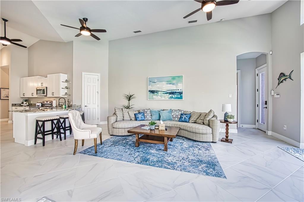 Living area featuring a ceiling fan, arched walkways, vaulted ceiling, and light marble finish floors