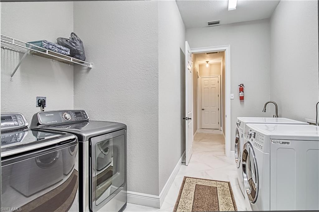 Laundry area featuring washing machine and clothes dryer, a textured wall, and light marble finish flooring