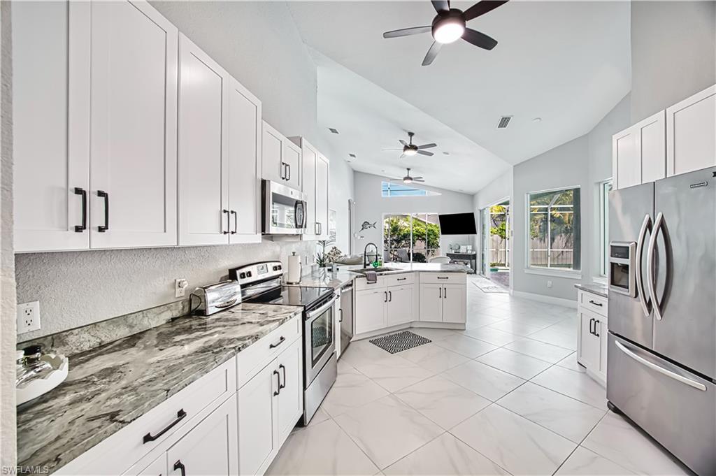 Kitchen with stainless steel appliances, white cabinets, a ceiling fan, a peninsula, and lofted ceiling