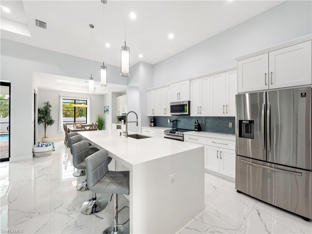 Kitchen featuring stainless steel appliances, a kitchen breakfast bar, a large island with sink, white cabinetry, and decorative light fixtures