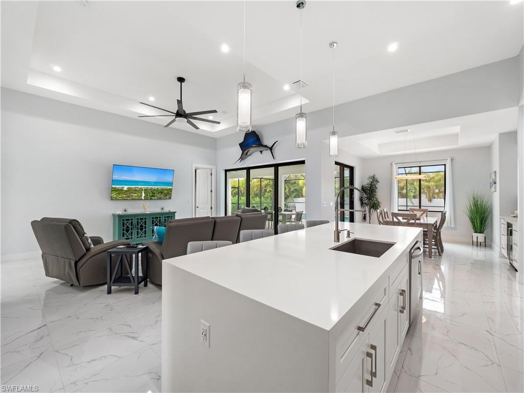 Kitchen featuring a raised ceiling, open floor plan, an island with sink, light stone counters, and hanging light fixtures