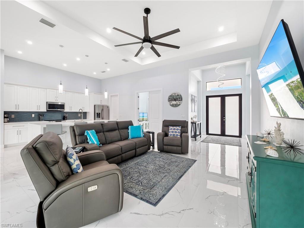Living area featuring french doors, ceiling fan, a tray ceiling, recessed lighting, and light marble finish floors