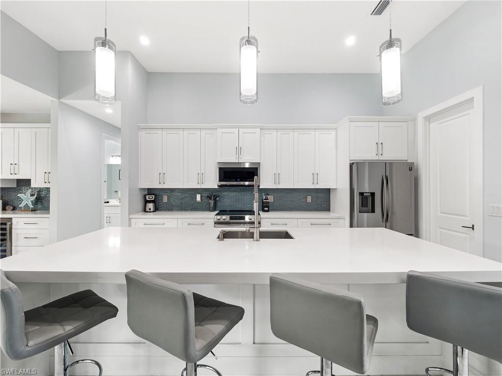 Kitchen featuring decorative backsplash, a kitchen breakfast bar, stainless steel appliances, and white cabinets