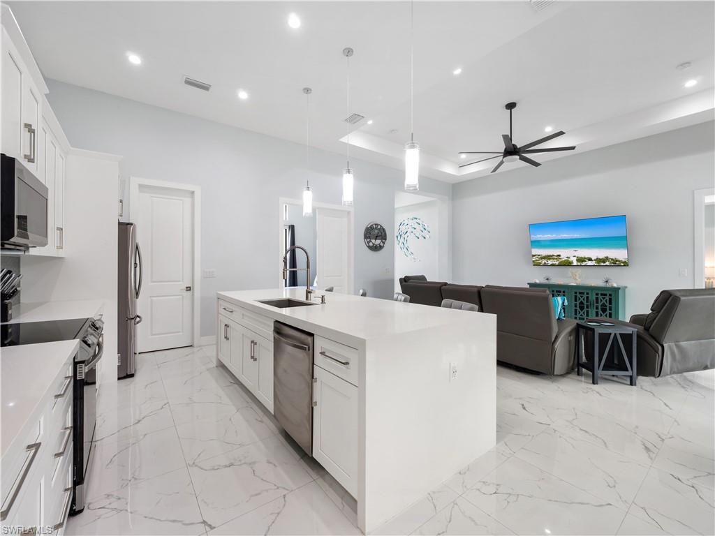 Kitchen featuring white cabinets, open floor plan, a kitchen island with sink, hanging light fixtures, and a tray ceiling
