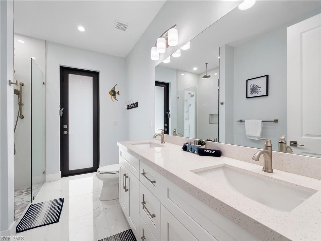 Bathroom with a marble finish shower, double vanity, and recessed lighting