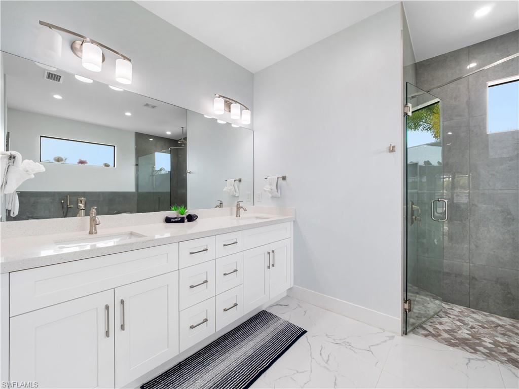 Full bathroom with double vanity, plenty of natural light, a stall shower, and light marble finish flooring
