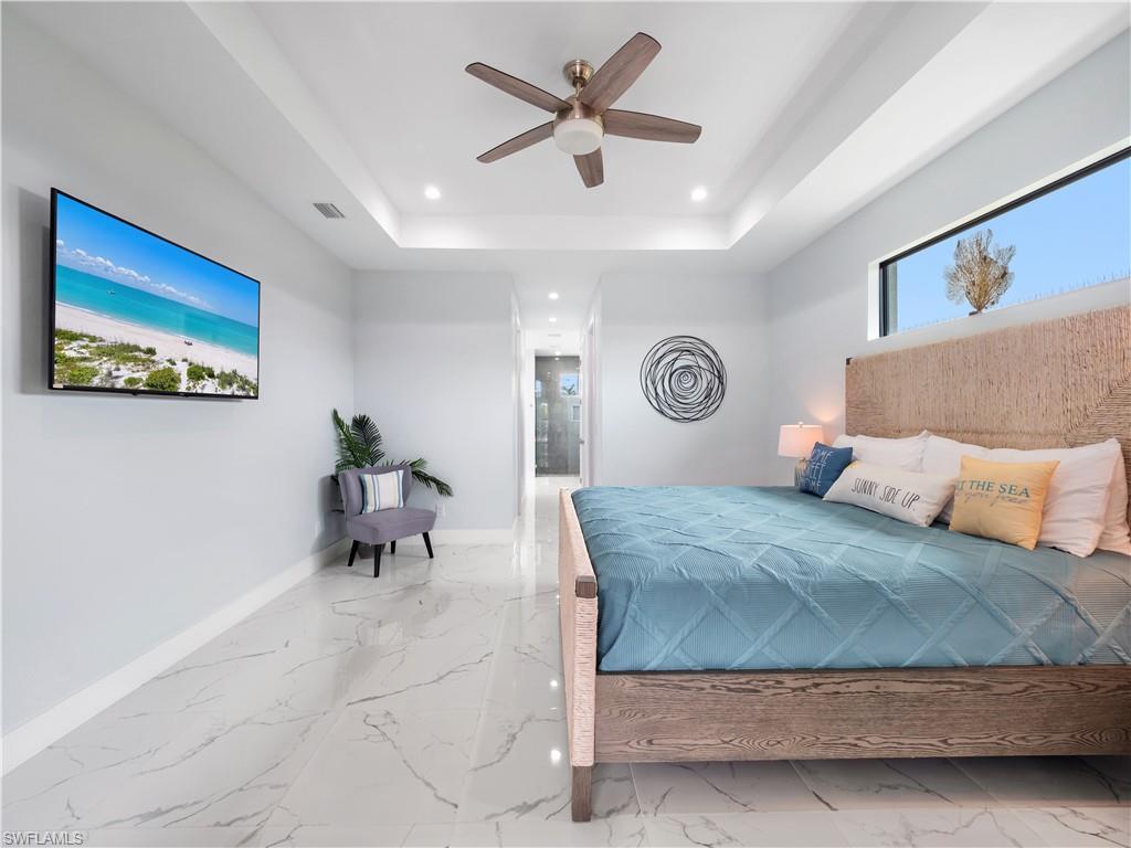Bedroom with ensuite bathroom, a ceiling fan, recessed lighting, a tray ceiling, and light marble finish flooring