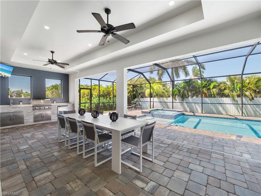 Fenced backyard with an outdoor kitchen / dining area, a patio, a pool with connected hot tub, a sunroom, and glass enclosure