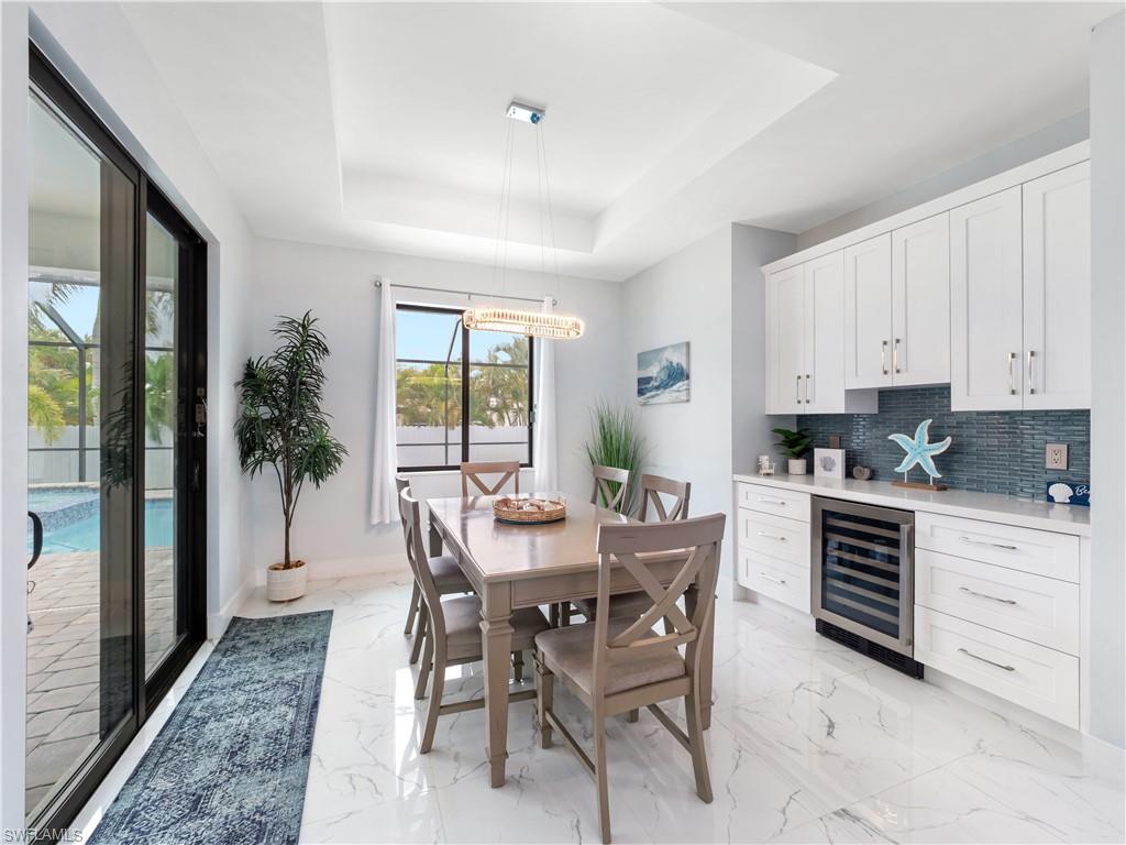 Dining area featuring beverage cooler, a raised ceiling, a chandelier, and light marble finish flooring