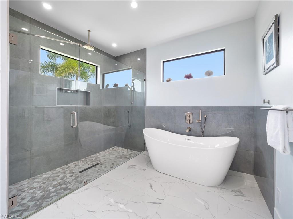 Bathroom featuring tile walls, healthy amount of natural light, marble finish flooring, a shower stall, and a freestanding tub