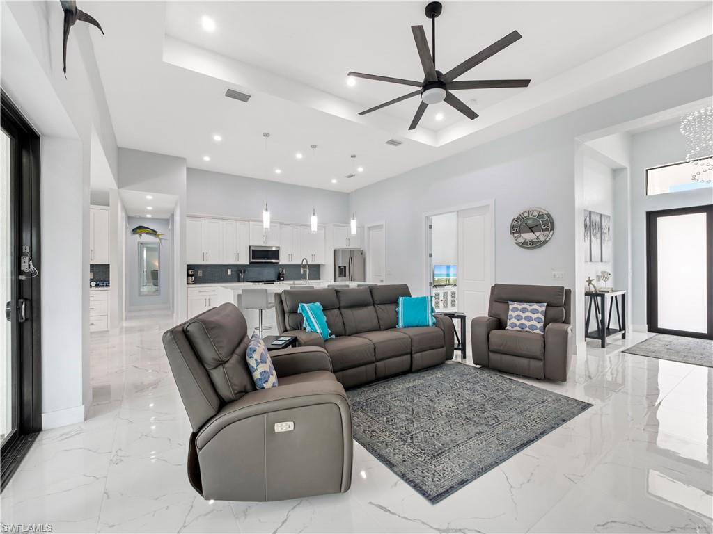 Living area with ceiling fan, light marble finish floors, a chandelier, and a raised ceiling