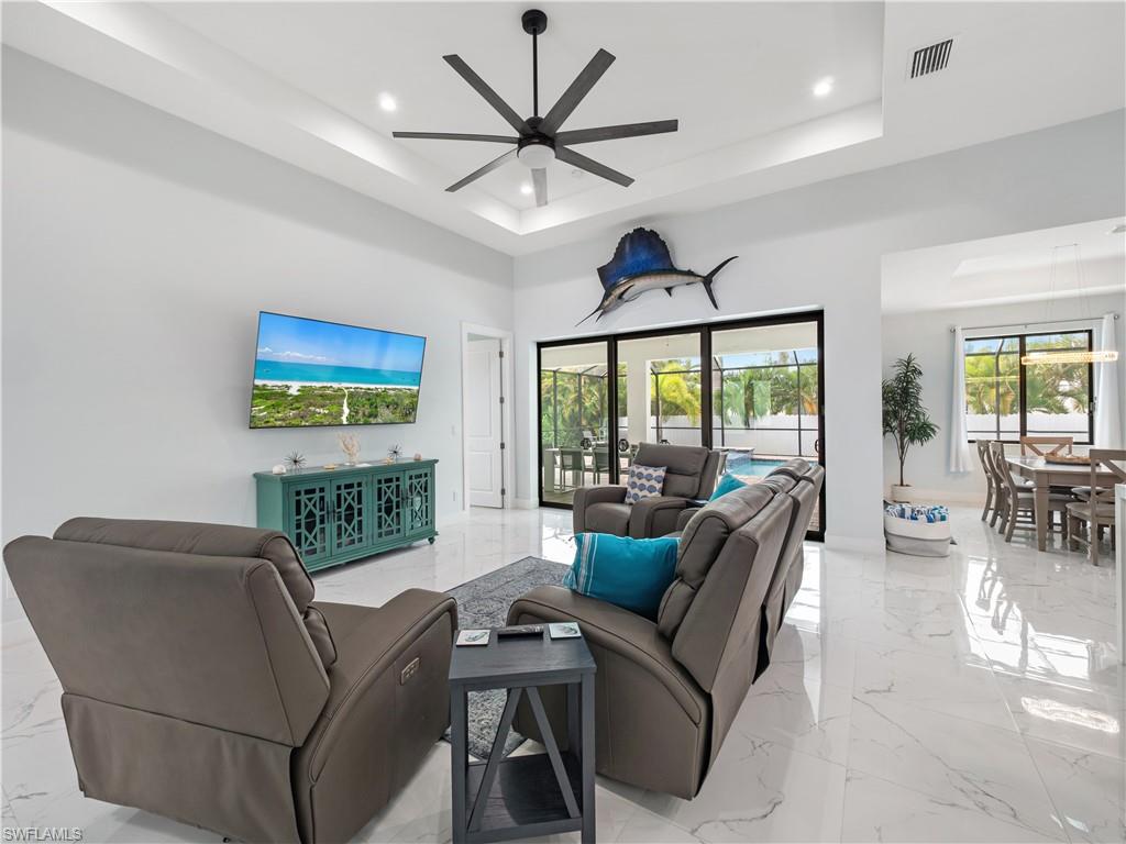 Living area featuring a ceiling fan, recessed lighting, a tray ceiling, and light marble finish flooring