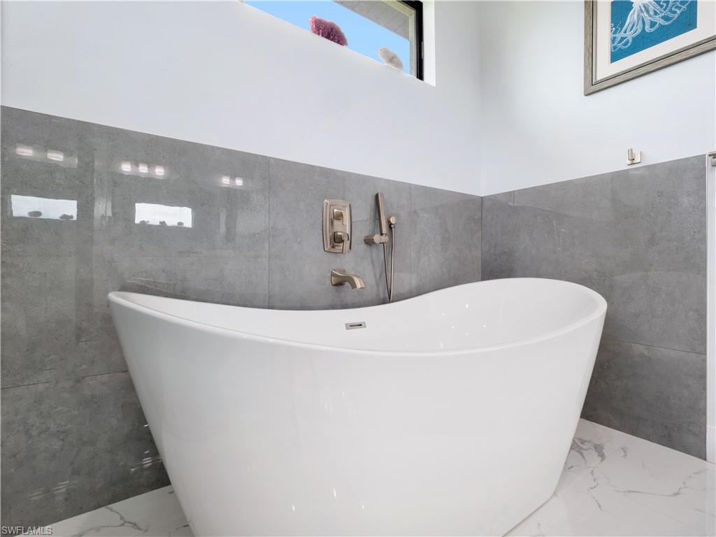 Bathroom with tile walls, a soaking tub, and marble tiled flooring