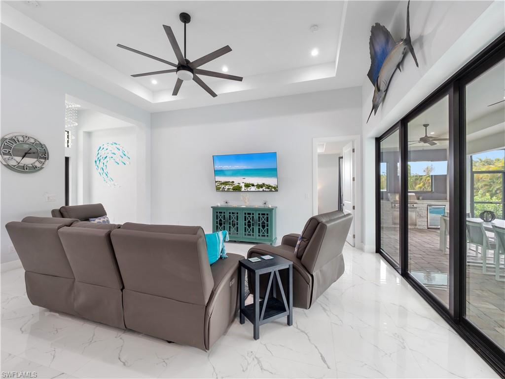 Living area featuring a ceiling fan, a raised ceiling, beverage cooler, recessed lighting, and light marble finish flooring