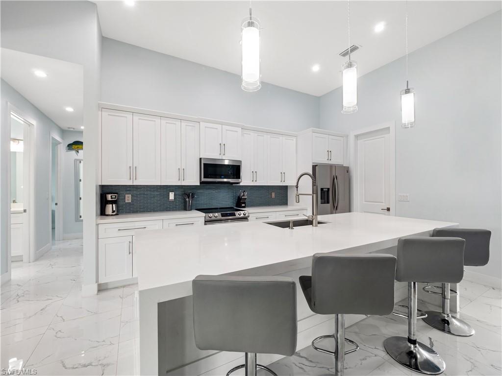 Kitchen featuring light marble finish floors, white cabinets, stainless steel appliances, a kitchen island with sink, and light stone counters