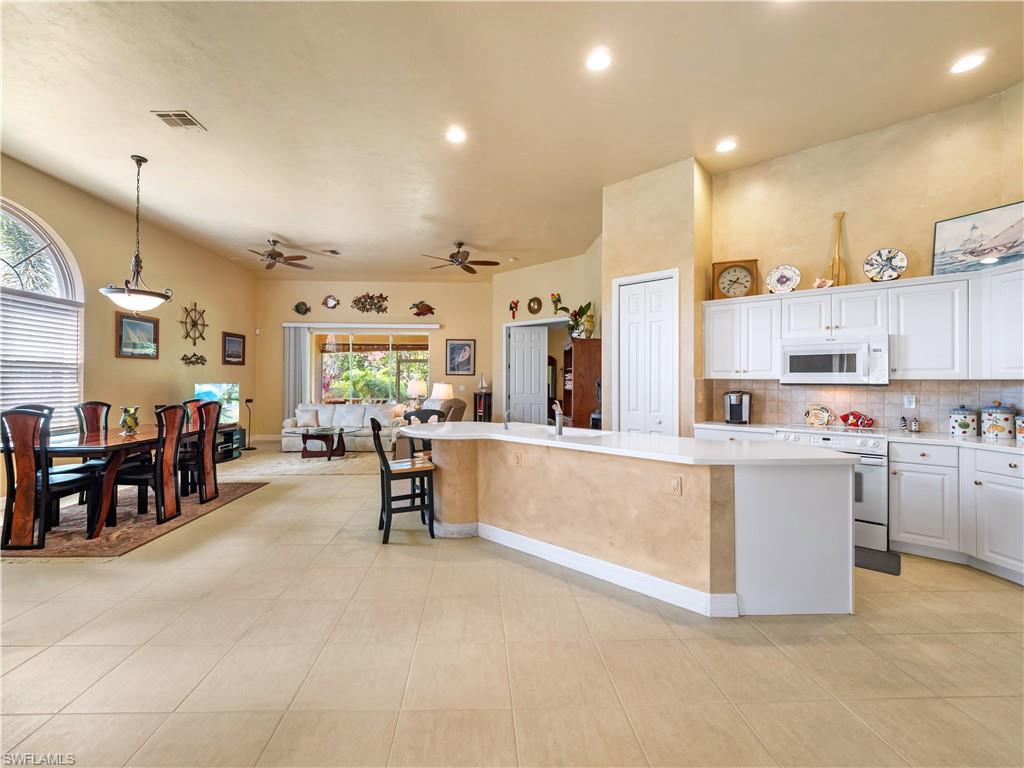 Kitchen featuring white appliances, tasteful backsplash, white cabinets, a large island with sink, and ceiling fan