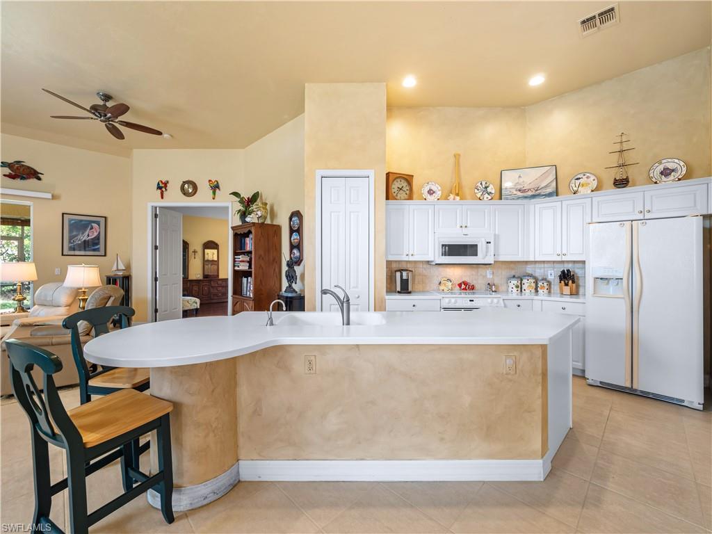 Kitchen with white appliances, white cabinetry, decorative backsplash, ceiling fan, and a large island with sink